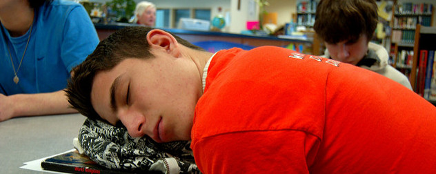 teenager sleeping on a table, using a bookbag for a pillow