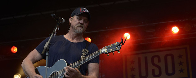 Trace Adkins plays guitar in front of a USO banner