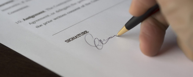 hand signing a legal document with a ballpoint pen