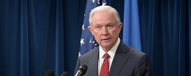 Jeff Sessions speaking at a podium in front of an American flag and a blue curtain