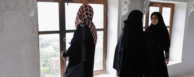 three women in Abayas and hijabs, two facing away from the camera and one facing toward