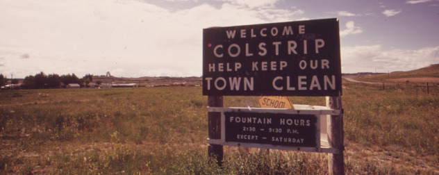 1973 photo of sign reading 'Welcome Colstrip Help Keep Our Town Clean' and fountain hours