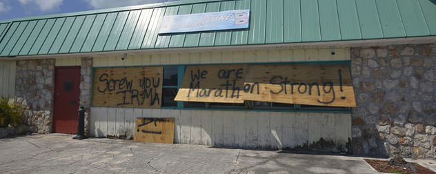 boarded-up storefront with the spraypainted message 'Screw you, Irma. We are Marathon strong!'