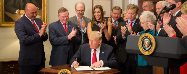 President Trump signs an executive order in the Roosevelt Room at the White House while observers applaud