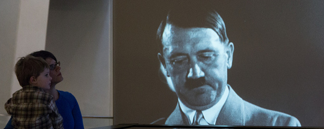 a woman and child looking at a video screen with an image of Hitler