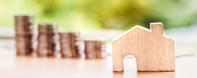 wooden block shaped like a house, with stacks of coins out of focus in the background