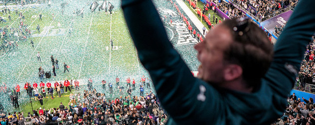 an Eagles fan celebrates in the foreground as confetti falls on the field after the 2018 Super Bowl