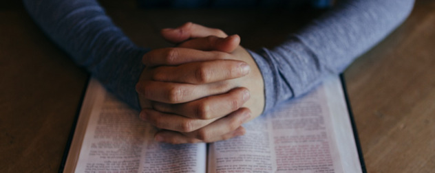 hands folded, as in prayer, resting on an open book