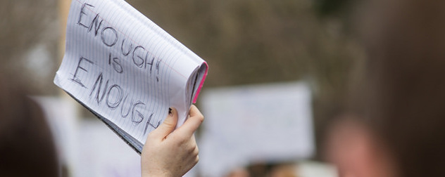 'ENOUGH IS ENOUGH' handwritten on the page of a notebook, held aloft