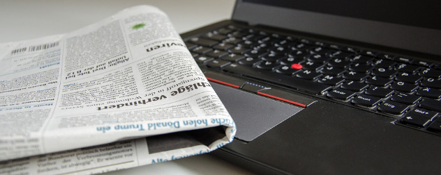 folded newspaper resting against an open laptop