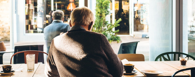 person with short, white hair seen from behind sitting at a table in a coffee shop