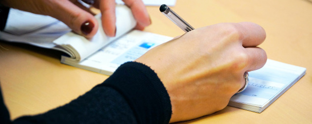 hands with nail polish and a ring writing out a paper check