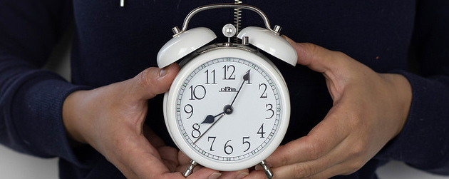 person holding an old-fashioned analog alarm clock just below chest height