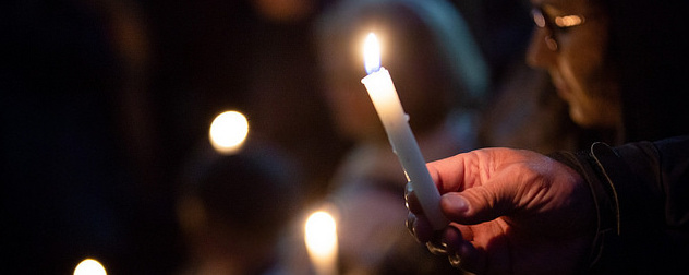 detail of someone holding a white taper candle at a candlelight vigil
