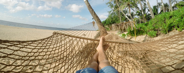 a person in jean shorts in a hammock on a tropical beach