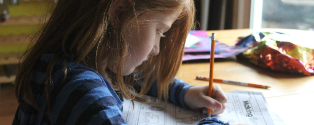 child with long hair works on homework worksheet at a table