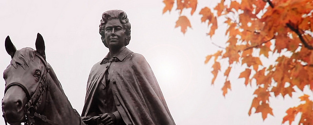 statue of Queen Elizabeth II on horesback, against a gray sky and orange autumn leaves.