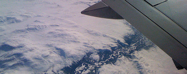 aerial view of a snowy landscape with a river, and part of a commercial airplane wing.