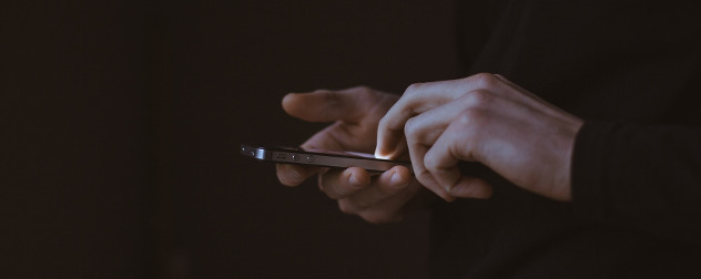 hands holding an illuminated smartphone in darkness.