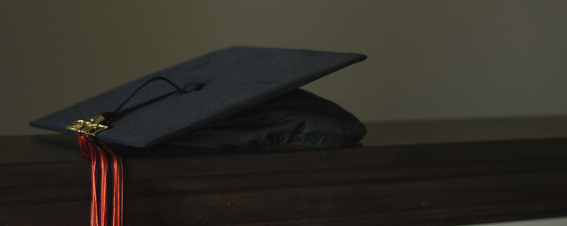 a black mortarboard graduation cap resting on a wood table against a dark background.