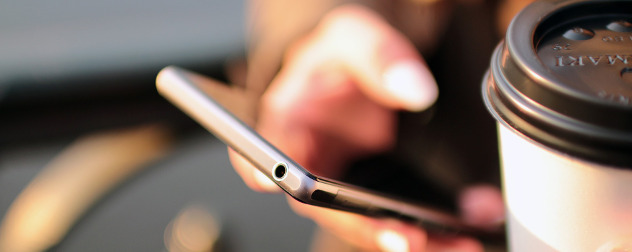 detail of person holding a smartphone next to a disposable cup of coffee.