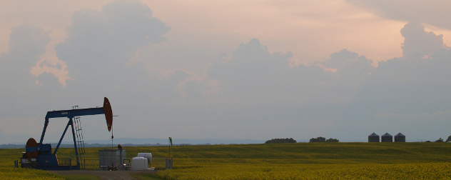 Alberta landscape with a pumpjack, grain silos and field against a sunset.