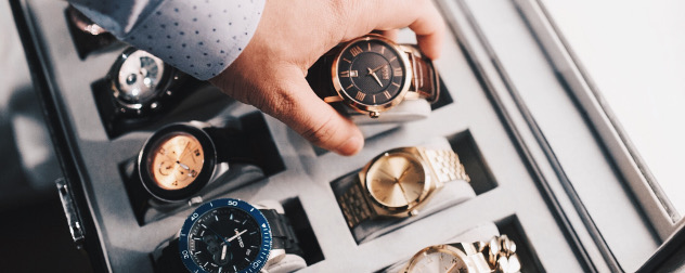 detail of hand removing one luxury watch from a case with several watches.