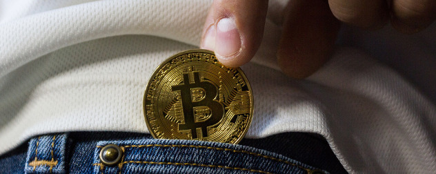 hand putting a physical representation of a bitcoin into a jeans pocket.