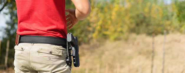 detail of a person with a red shirt and khakis wearing a handgun in a hip holster.