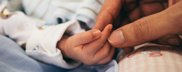 detail of adult hand and baby hand against blankets.