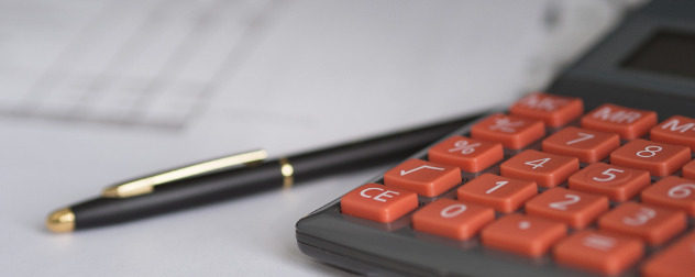 detail of a calculator, with a ballpoint pen and papers out of focus in the background.