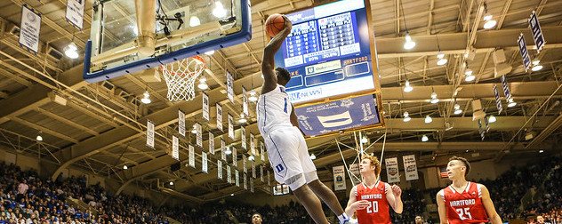 Zion Williamson, midair, about to make a basket as opposing players look on.