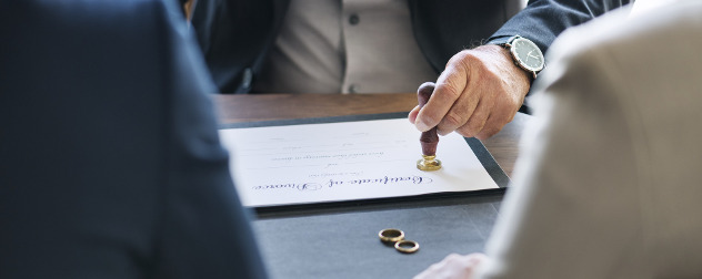 person impressing a seal on a certificate of divorce, while two others watch, wedding rings resting nearby.