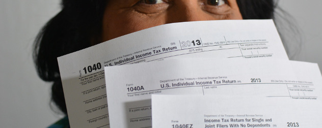 person holding paper versions of IRS Form 1040, 1040A and 1040EZ in front of their face, mostly obscuring it.