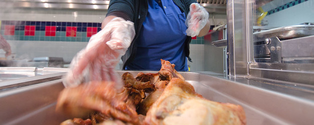 cafeteria worker putting roasted chicken in a heating tray (detail).