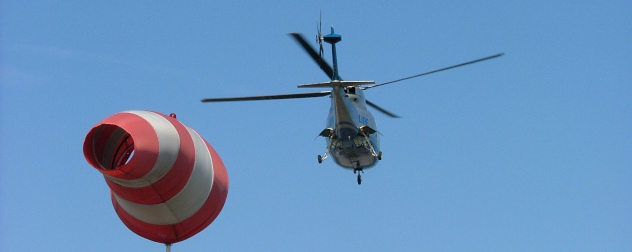 Sikorsky S-76C helicopter flying away, wind sock in foreground.