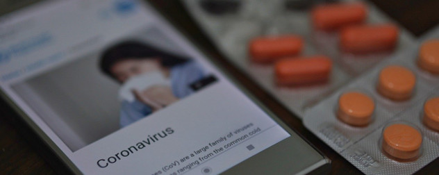 phone displaying information about the coronavirus, with blister packs of pills.