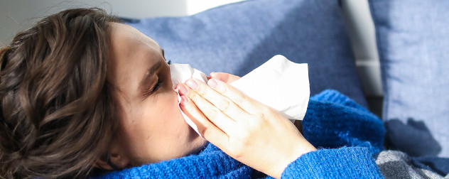 detail of person with long hair blowing their nose into a tissue, who might need paid leave from work.