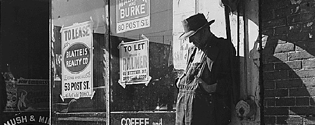 black and white image of a man in a hat and overalls leaning against a store covered in 'to lease' signs, among Depression-era heavy unemployment.