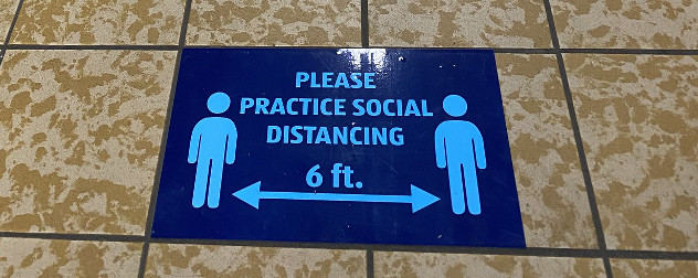 grocery store sign that reads 'please practice social distancing' with two people separated by 6 feet.