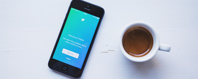 phone displaying Twitter app next to a cup of coffee.