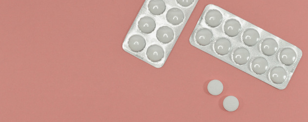 white, round tablets in blister packs against a pink background.