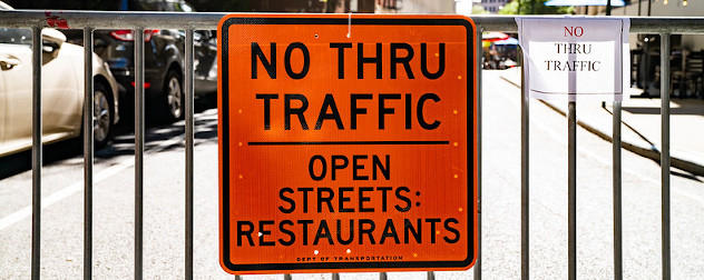 sign on a barricade that reads 'No Thru Traffic, Open Streets, Restaurants.