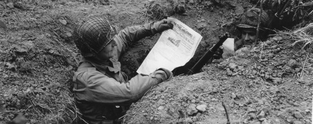 Two WWII GIs in a foxhole, one reading an issue of Stars and Stripes and the other reading mail.