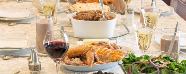 detail of a Thanksgiving dinner table with table settings, turkey, wine, stuffing and chocolate milk.