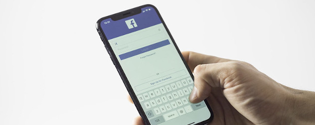 Apple iPhone displaying the Facebook app, held in a hand.
