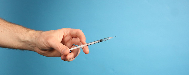 hand holding a syringe against a blue background.