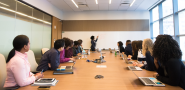 group of people working at a conference table, one person standing at whiteboard.