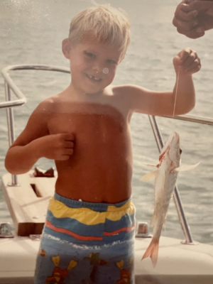 young Anthony Criscuolo showing off a fish on a boat.