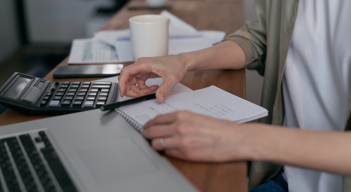 detail of person's hands with laptop, calculator, pen and notepad.